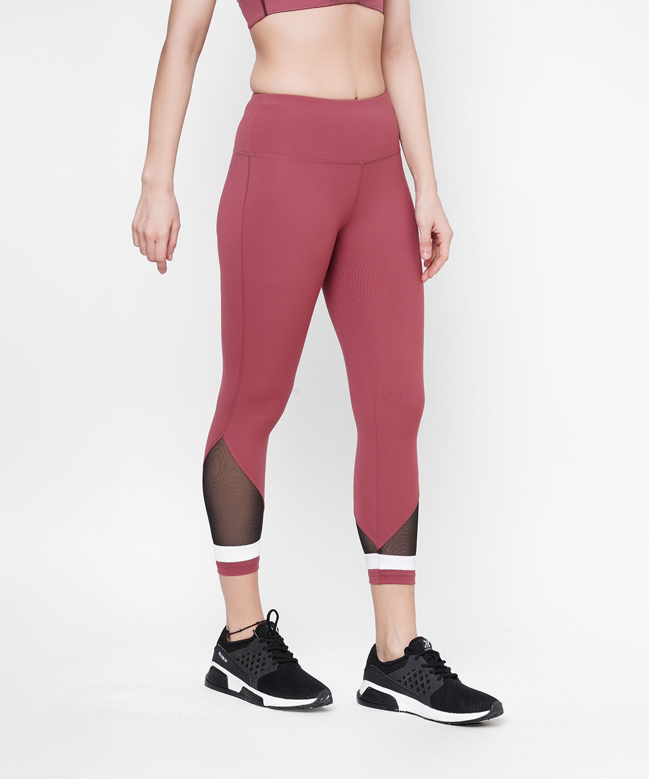 A woman wears the Punch Pink Capri with a compression-fit waistband and mesh panels, paired with black sneakers, standing against a white background.