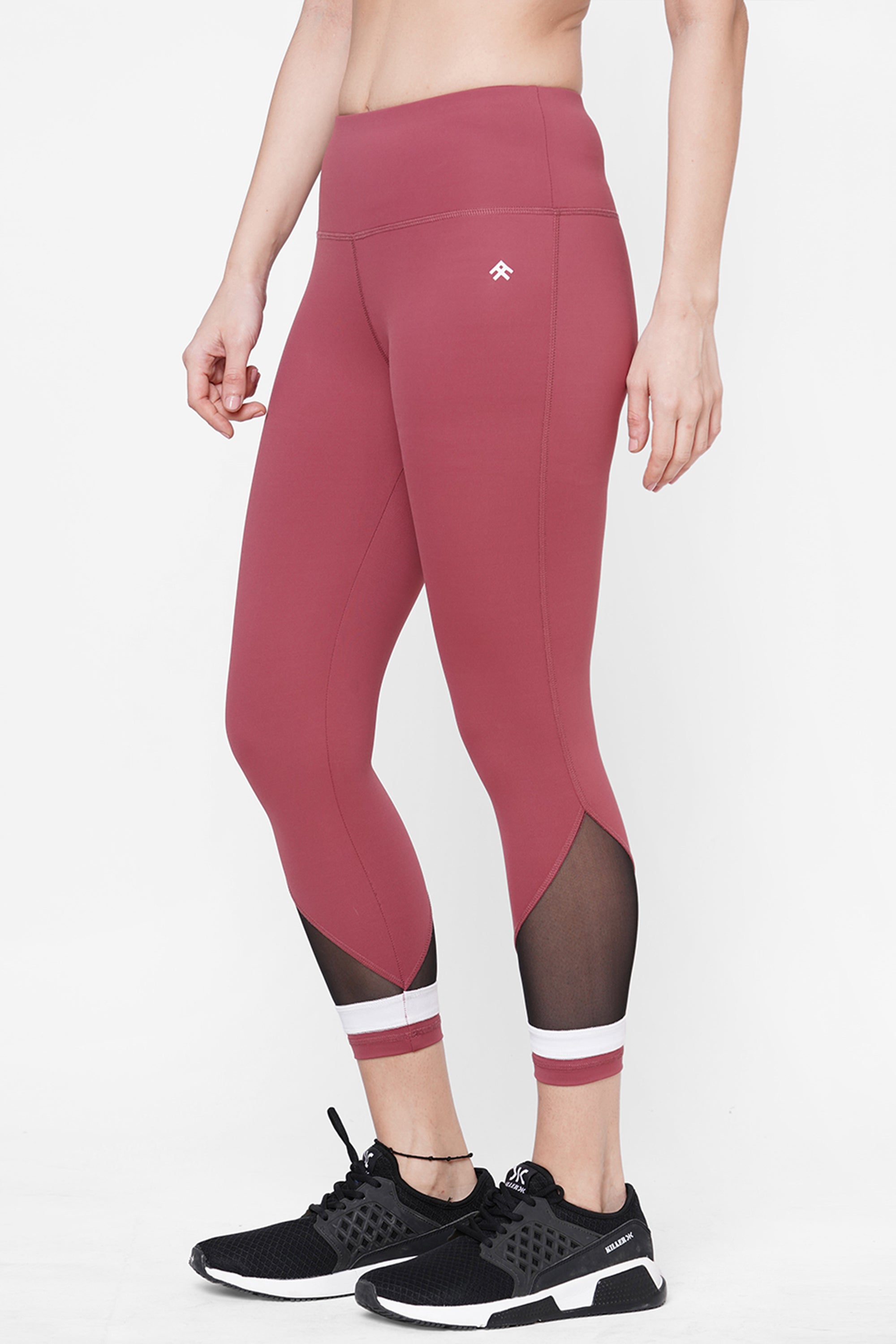 A person stands sideways in Punch pink Capri leggings featuring a high-waisted compression fit and black mesh panels, paired with black sneakers—a stylish workout clothing choice.