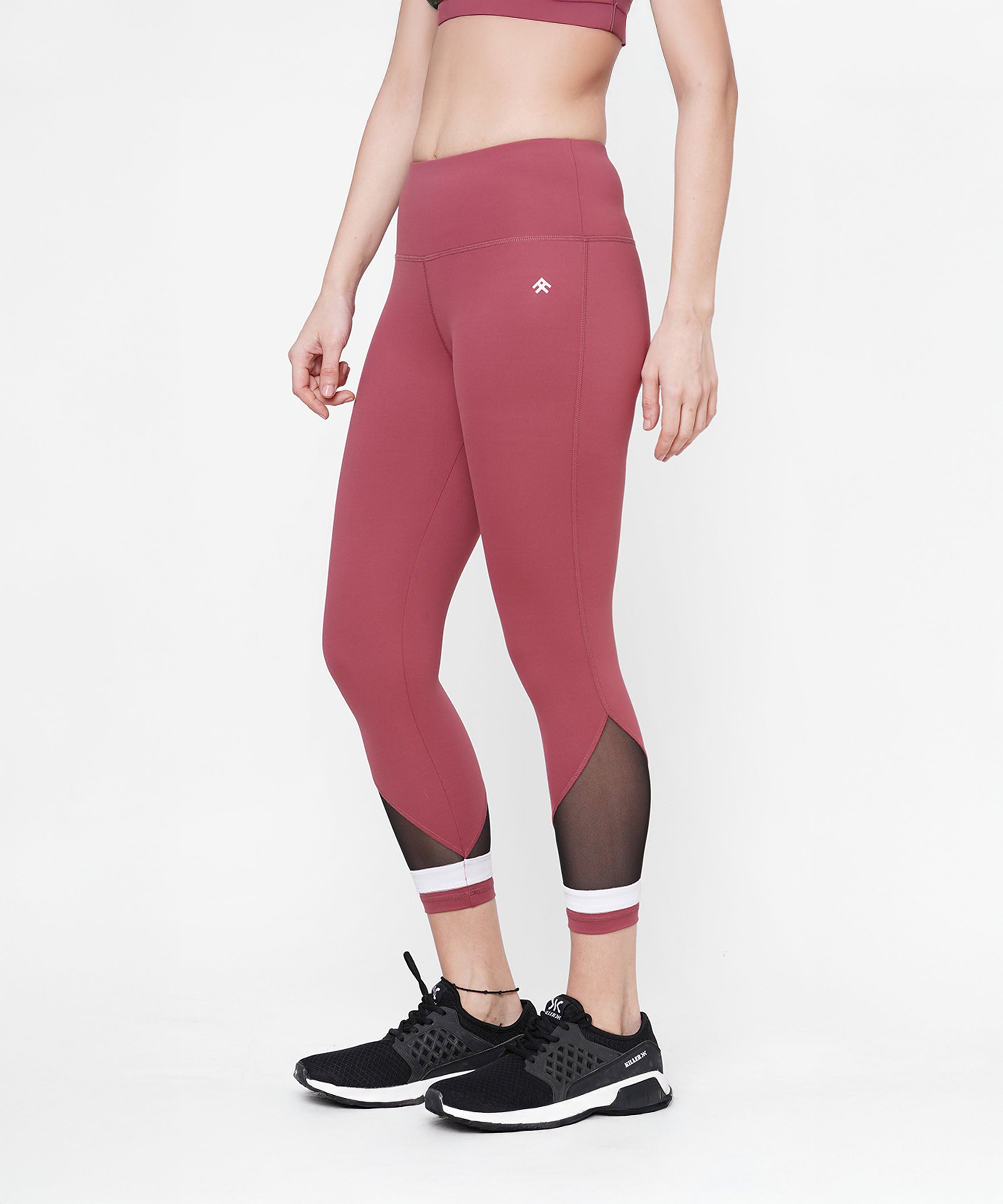 Woman modeling Punch Pink Capri leggings with mesh panels and a compression-fit waistband, paired with black sneakers. Shown from midriff down.