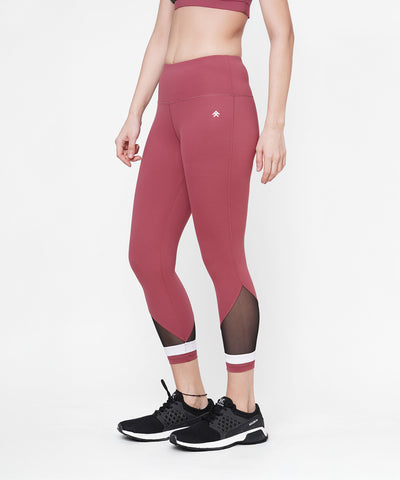 Woman modeling Punch Pink Capri leggings with mesh panels and a compression-fit waistband, paired with black sneakers. Shown from midriff down.