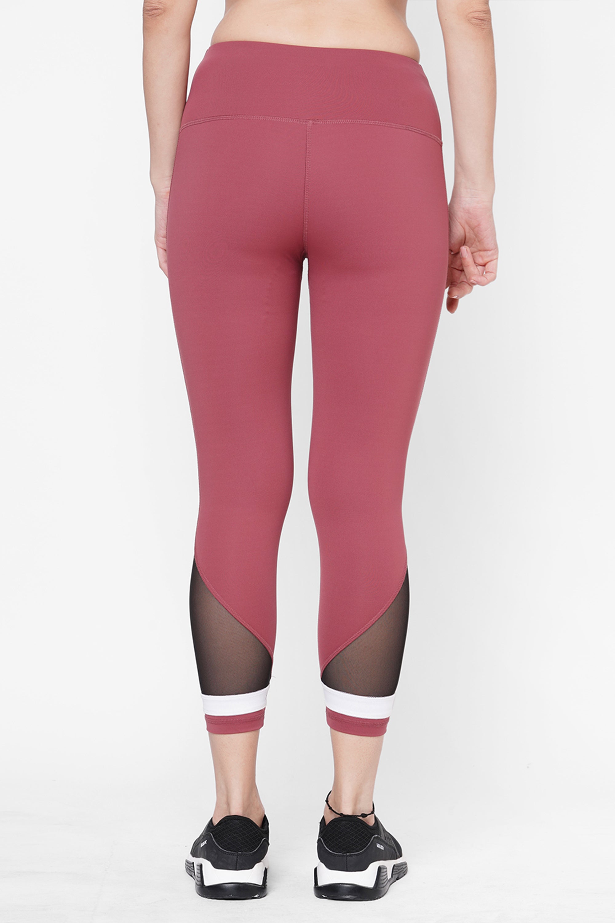 Person seen from the back wearing Punch Pink Capri leggings featuring a compression fit waistband, black mesh panels, and white-striped ankles—a stylish workout look.