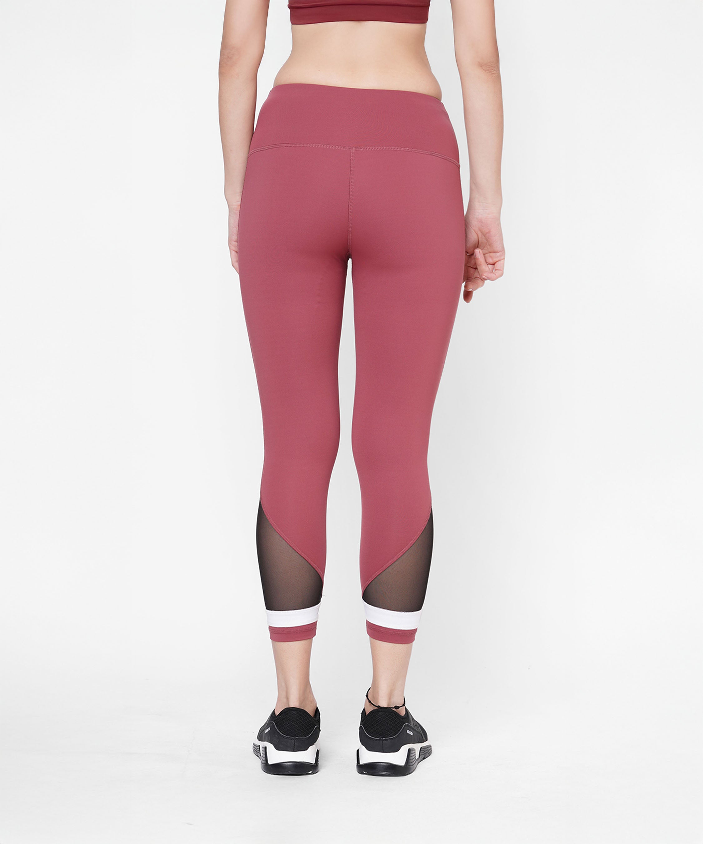 Woman wearing Punch Pink Capri with mesh panels and a compression fit waistband, paired with sneakers, shown from the back against a white background.