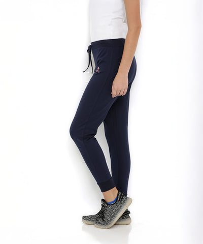 A woman in a white T-shirt and Blue Classic Joggers TLC04 with a slim tapered fit, paired with black sneakers, stands against a white background.