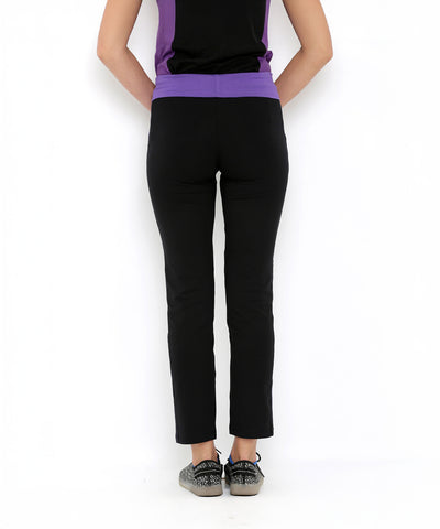 A woman stands against a white background, seen from behind, wearing Regular Fit Trackpants TLC05 in black with a purple top and sneakers.