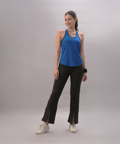 Smiling woman wears a Blue Racer Back Top and black slit-hem pants against a plain light background.