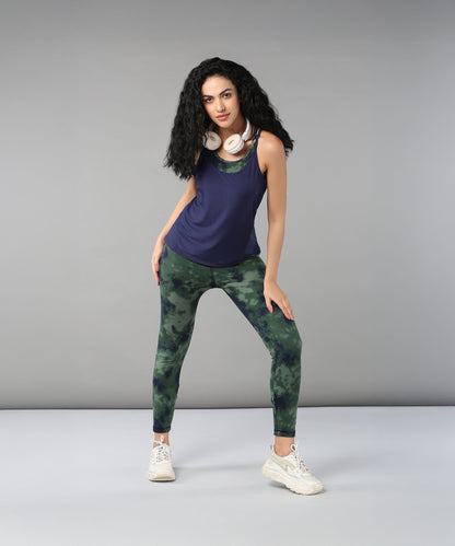A woman with curly hair wears headphones, a Tie & Dye Bra T shirt, green leggings, and white sneakers as she poses confidently.