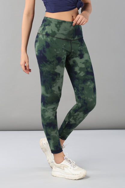 Woman in Tie & Dye Leggings made from stretchy fabric, paired with white sneakers and a blue cropped top, stands before a gray background—these leggings offer a stylish and comfortable upgrade to your workout wardrobe.
