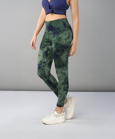A woman models the Tie & Dye Leggings in green, made from stretchy fabric, paired with a navy crop top and white sneakers against a gray background—ideal for updating your workout wardrobe.