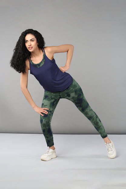 A woman in athletic wear does a side stretch against a gray background, highlighting her Tie & Dye Leggings made from stretchy fabric.