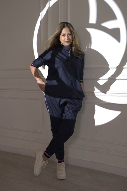 A woman in the Accented Set, a navy cotton co-ord, stands against a white wall with circular shadow patterns, hands in pockets.