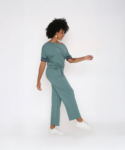 A woman exudes effortless style in the Sporty Sage Green Off-shoulder Tracksuit Set, a chic women’s co-ord with a standout off-shoulder design.
