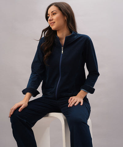 Woman wearing a Blue Denim Wash Jacket sits comfortably on a white stool, looking to the side and smiling.