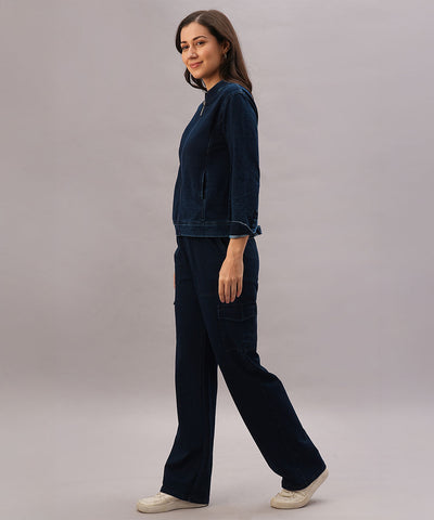A woman stands sideways against a plain light background, wearing the Blue Denim Wash Jacket and white sneakers.