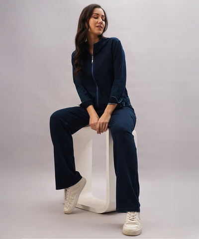 Woman in a navy blue tracksuit and white sneakers sits on a white stool, effortlessly layering her look with the Blue Denim Wash Jacket against a plain background.