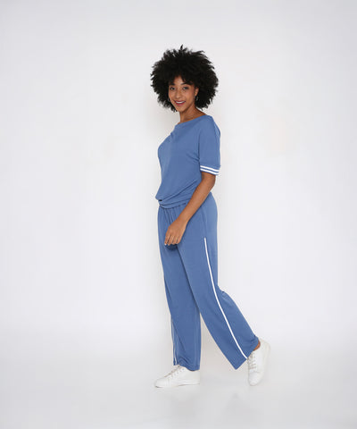 Woman models the Sporty Atlantic Blue Off-Shoulder Tracksuit Set with white sneakers, smiling against a plain white background.