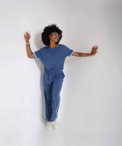 A woman poses playfully against a plain white background in the Sporty Atlantic Blue Off-Shoulder Tracksuit Set, paired with white sneakers.