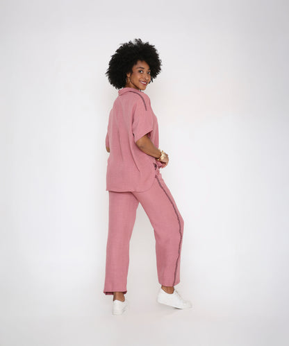 A woman smiles and looks over her shoulder in the Vintage Pink Loose Shirt and Pant Cord Set, made from soft viscose cotton, styled with classic white sneakers against a white background.