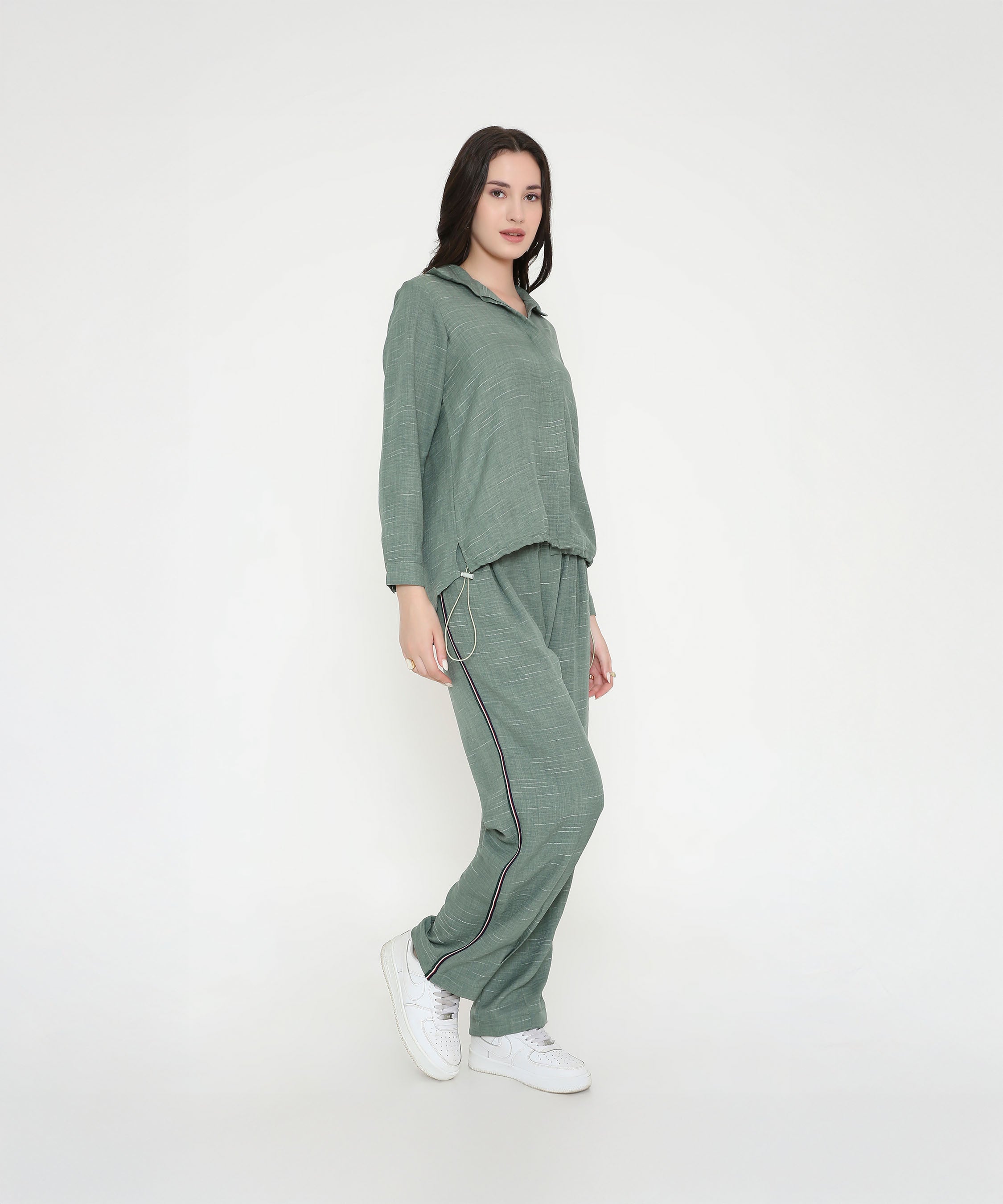 A woman in the Moss Green Breezy Cord Set pairs it with white sneakers, showcasing a relaxed loungewear look against a plain white background.
