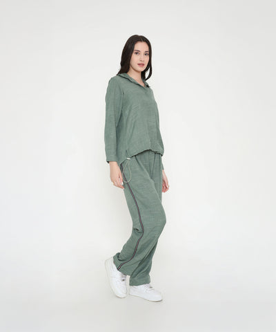 A woman in the Moss Green Breezy Cord Set pairs it with white sneakers, showcasing a relaxed loungewear look against a plain white background.