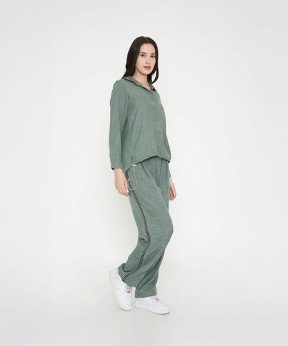A woman in the Moss Green Breezy Cord Set pairs it with white sneakers, showcasing a relaxed loungewear look against a plain white background.