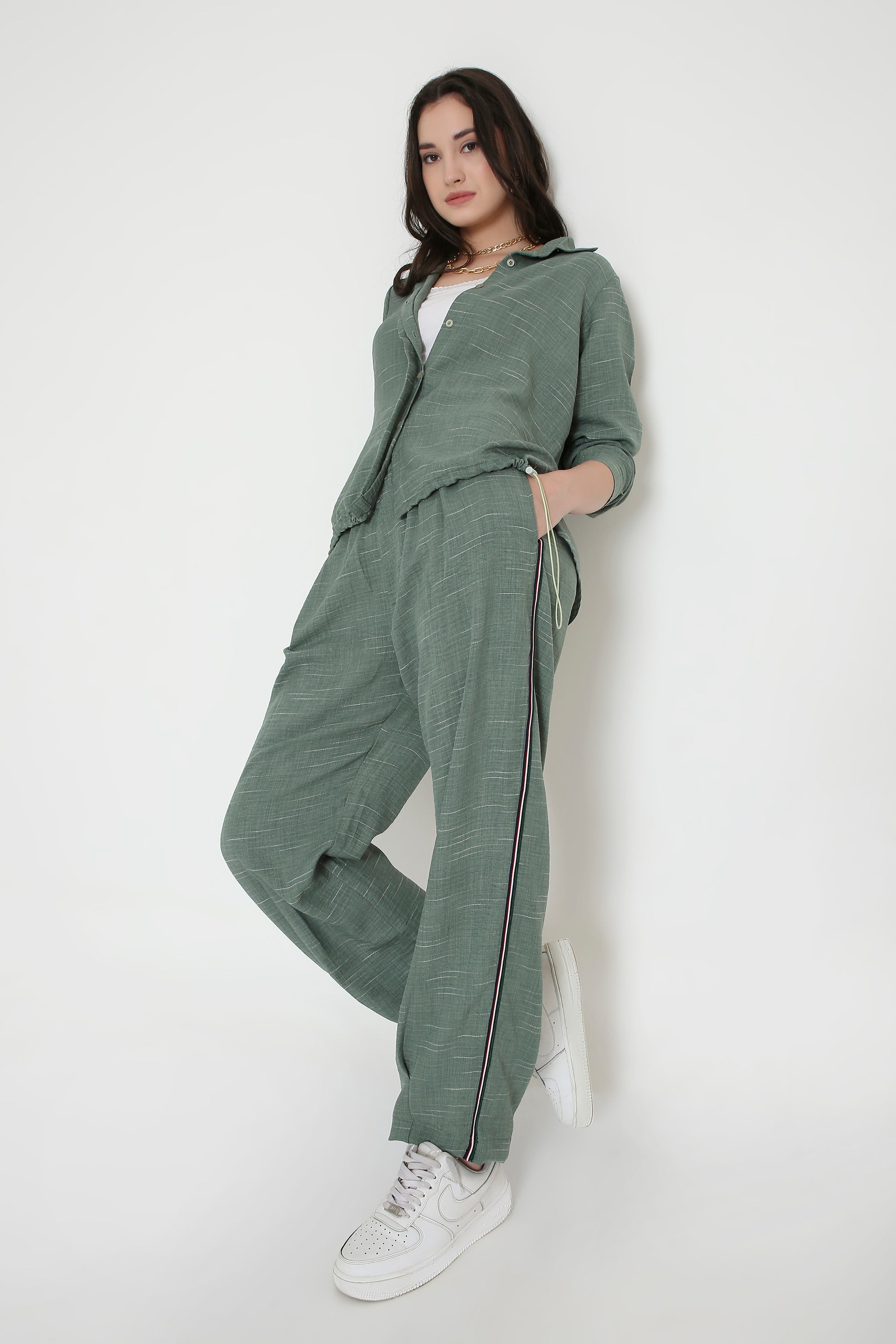 A woman models the Moss Green Breezy Cord Set, featuring a relaxed-fit pantsuit and white sneakers, posing against a plain white background.