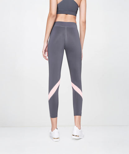 A woman stands facing away on a plain light background, wearing Grey Leggings featuring pink stripes and color-block panels.