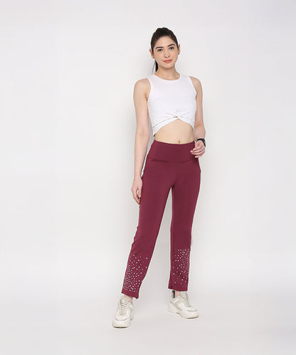 Woman in a White Twisted Crop Top and maroon pants with white sneakers stands against a plain white background.