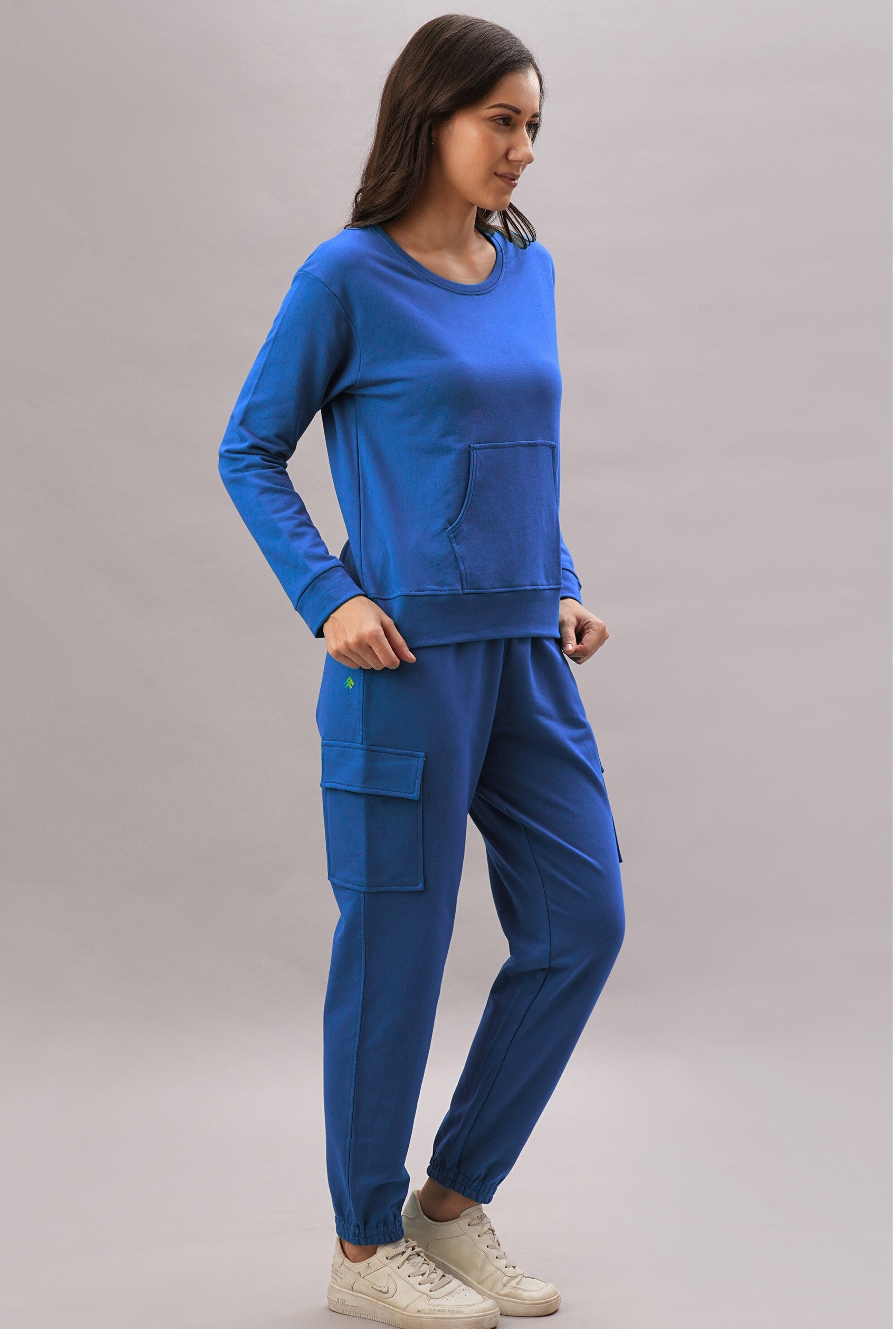 A woman stands sideways wearing the Soft Royal Blue Trackset, featuring long sleeves and cargo joggers, paired with white sneakers. Made from a soft cotton viscose blend for all-day comfort.