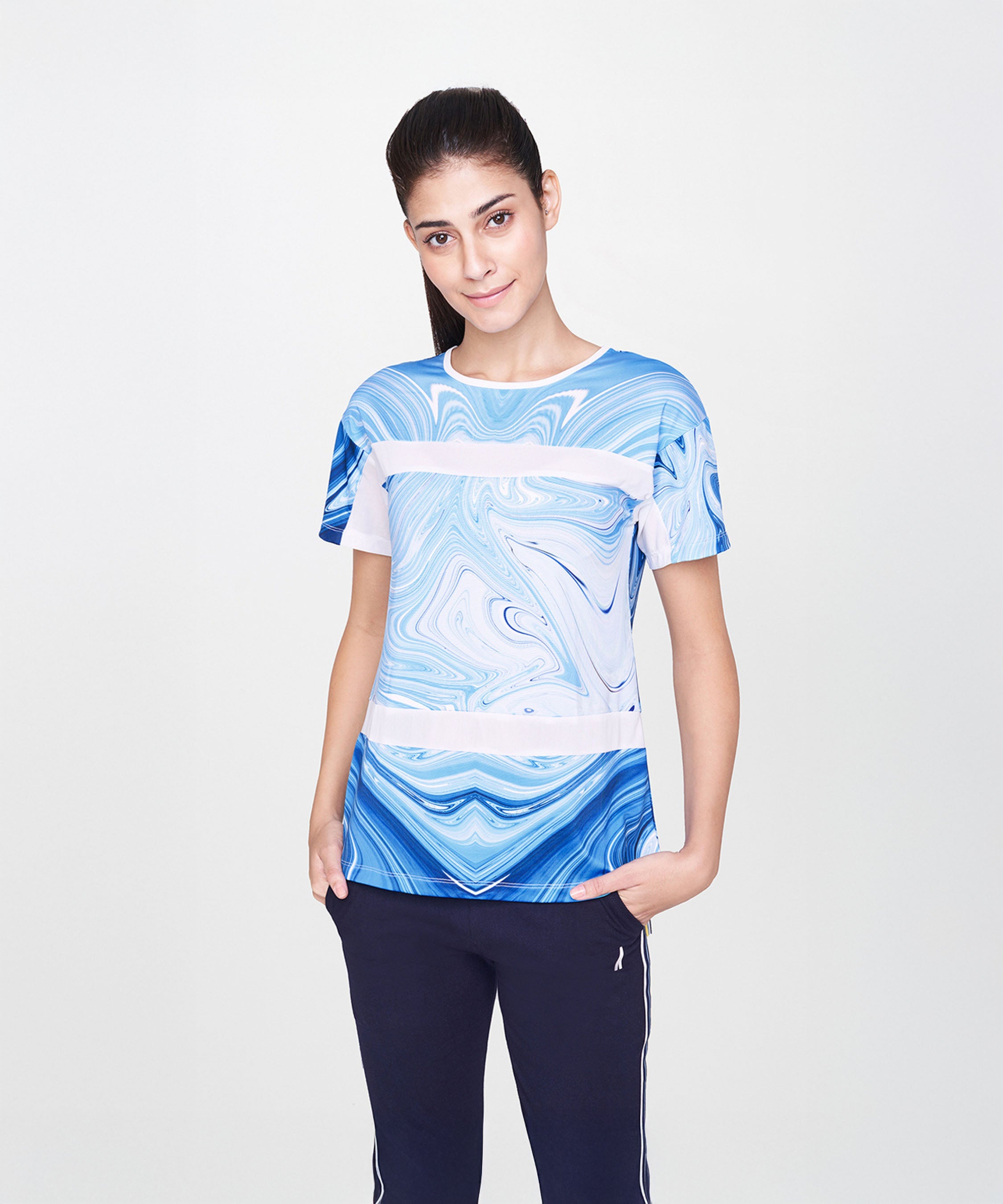 Woman smiles in a Sky Blue T-Shirt with a blue and white marble print and black pants, standing with one hand in her pocket.