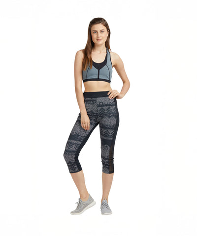 A woman poses confidently in Printed Capri track pants and sneakers on a white background, highlighting the stylish design.