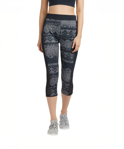 Woman styled in Printed Capri black patterned cotton-spandex cropped leggings and a black top, paired with gray sneakers, stands against a white background.