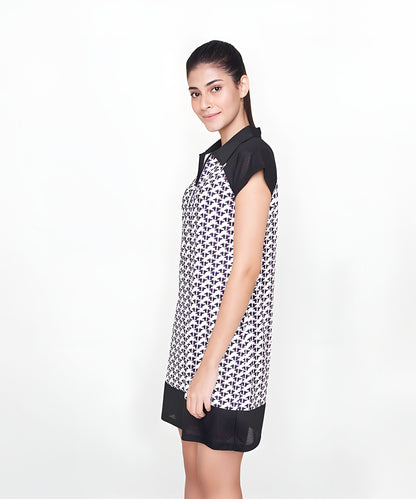 A woman stands sideways in a Black Dress with a white collar, crafted from polyester—an ideal effortless airport look—against a simple background.