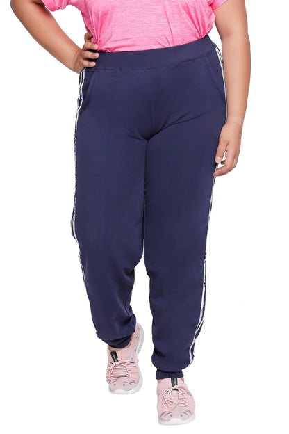 A person wears the Joggers With Side Stripe - Plus Size in navy blue, featuring white side stripes, paired with a pink t-shirt and sneakers—made from high-stretch fabric for comfort and easy movement.