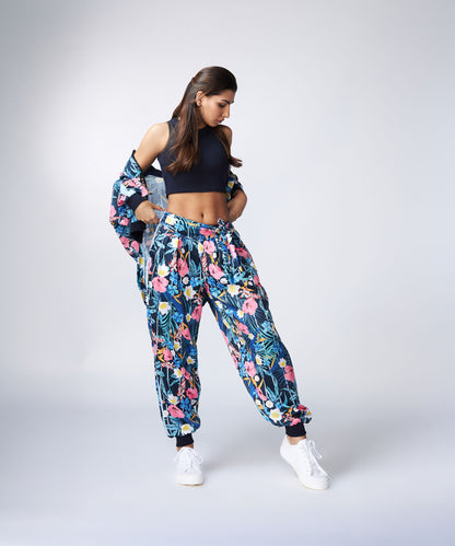 Woman in a sleeveless Navy Blue Crop Top, floral print pants and jacket, and white sneakers poses against a plain background.