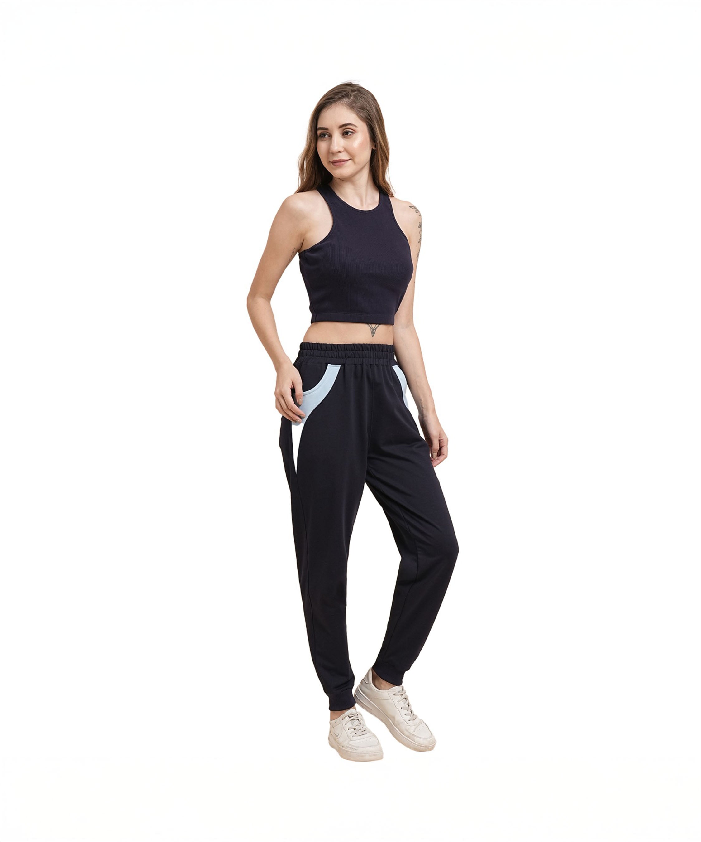Woman in a black sleeveless crop top, Tuna Active Navy Blue Joggers, and white sneakers stands and smiles.