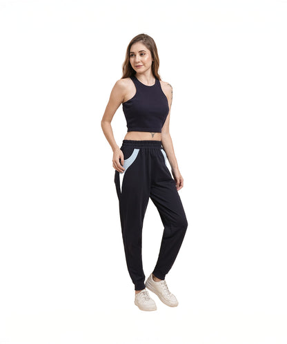 Woman in a black sleeveless crop top, Tuna Active Navy Blue Joggers, and white sneakers stands and smiles.