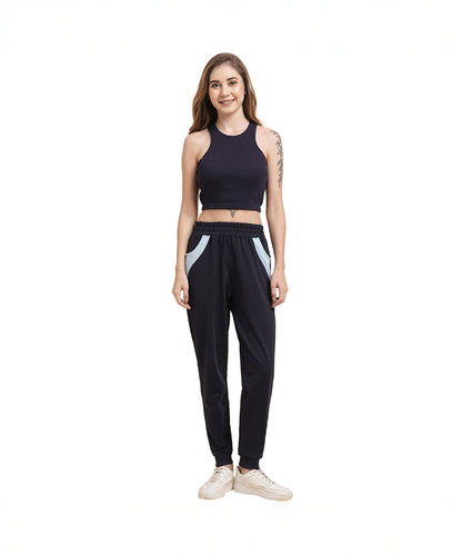 Woman in a black crop top and Tuna Active Navy Blue Joggers with white sneakers, standing and smiling against a white background.