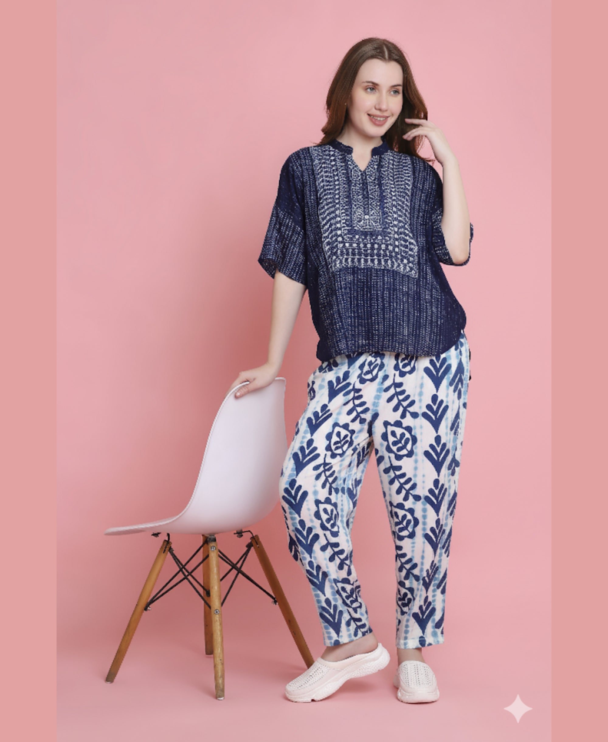 Woman in the Indigo Printed Top with Tie Dye Printed Pant Lounge Set stands beside a pink chair against a pink background.