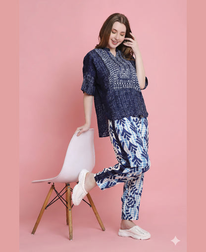 Woman in an Indigo Printed Top with Tie Dye Printed Pant Lounge Set poses by a white chair against a pink background.