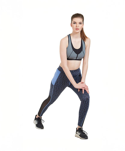 Woman in athletic wear does a side lunge stretch against a plain white background, highlighting the Blue Poly Cotton Lycra Printed Slim Fit Track Pant for Women with its stylish design and breathable comfort.