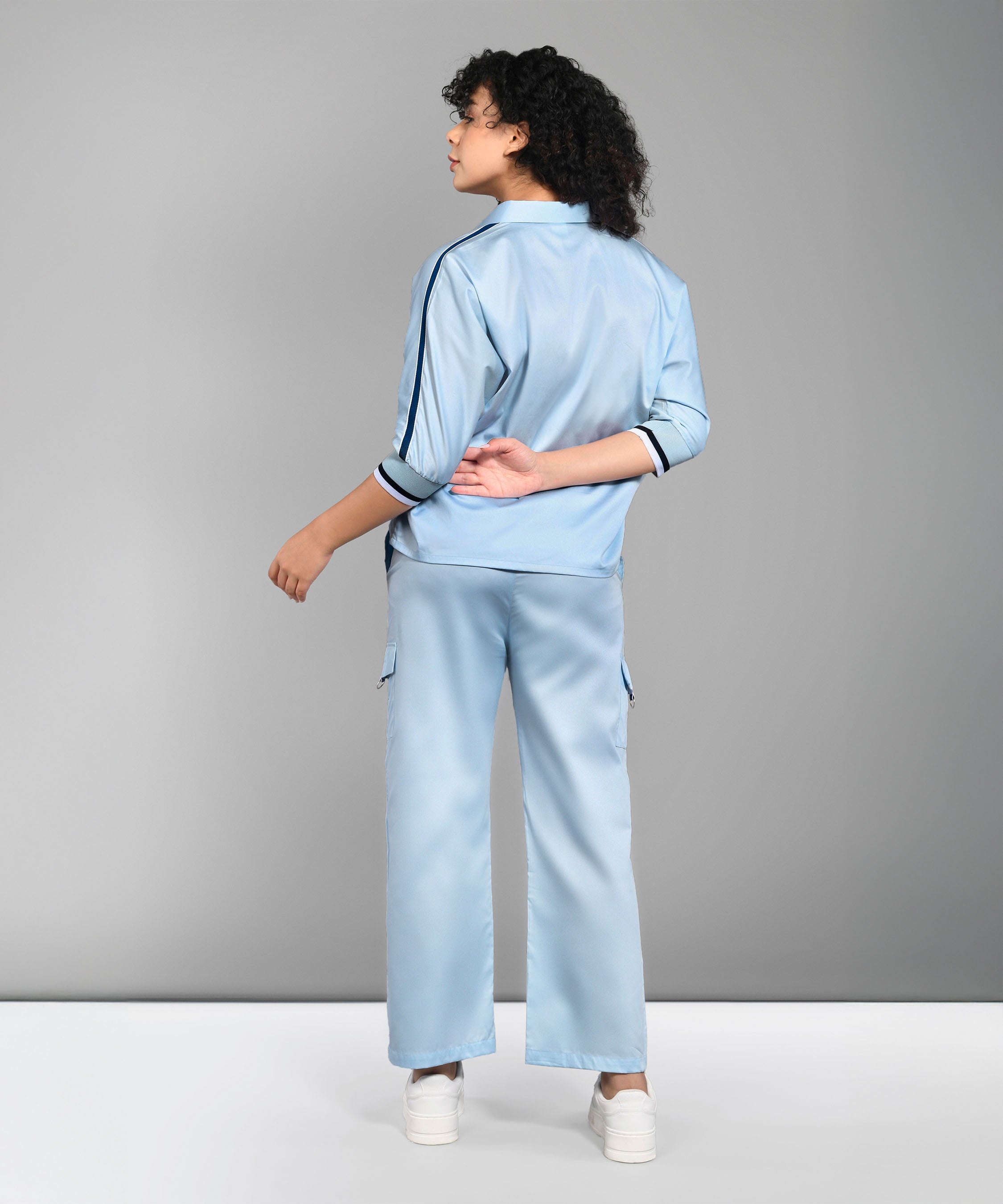 A person wearing the Denim Chic Set, featuring a light blue batwing sleeve shirt and cargo track pant, paired with white sneakers, stands with their back to the camera.