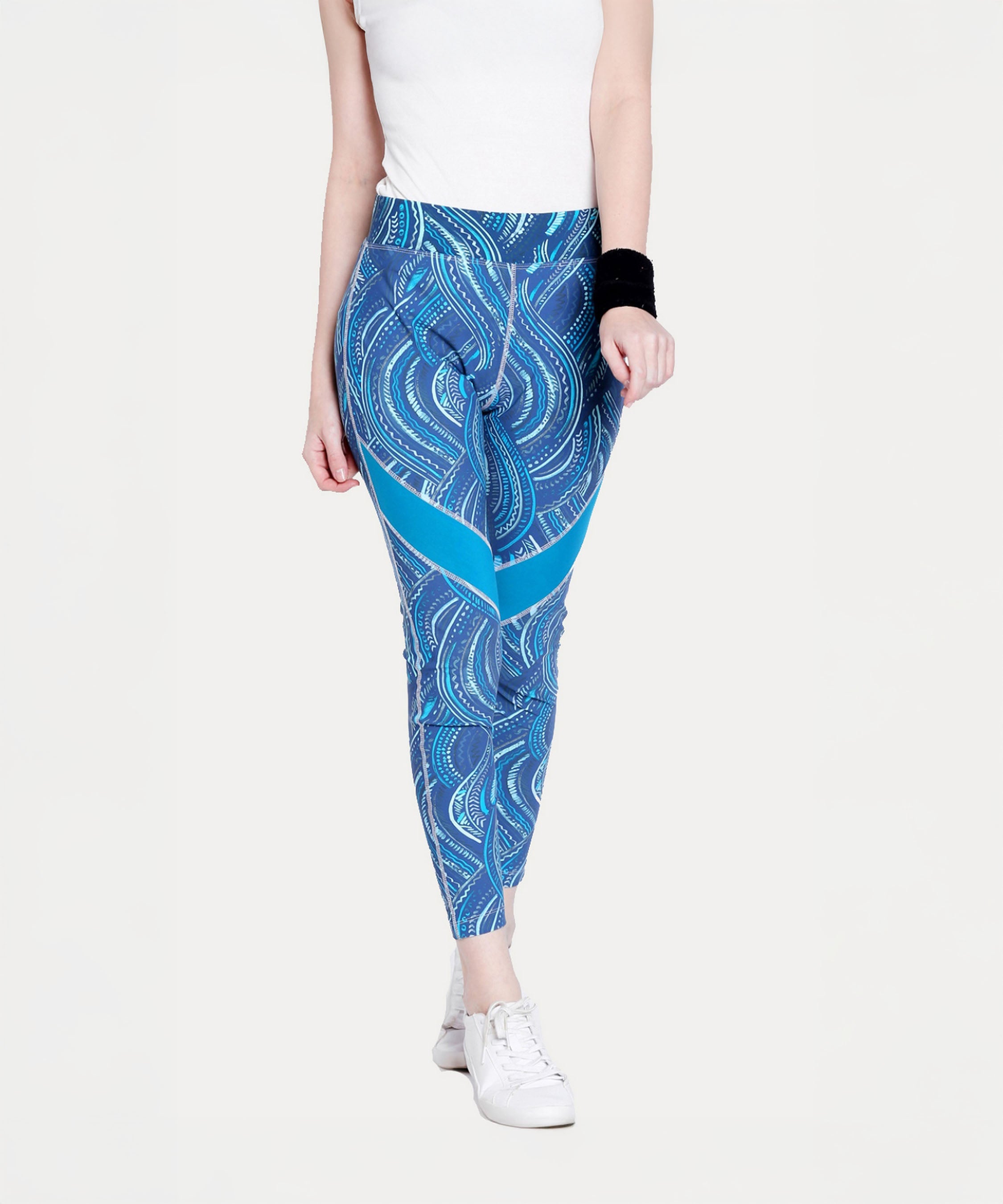 A woman walks forward in a white top and Tuna Active Printed Blue Leggings, paired with white sneakers and a black wristband.