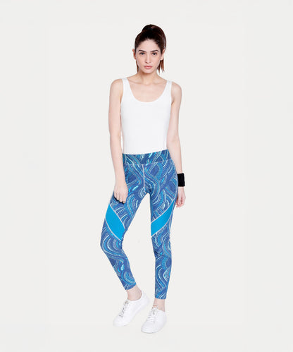 A woman in a white tank top wears Tuna Active Printed Blue Leggings while standing against a plain white background.