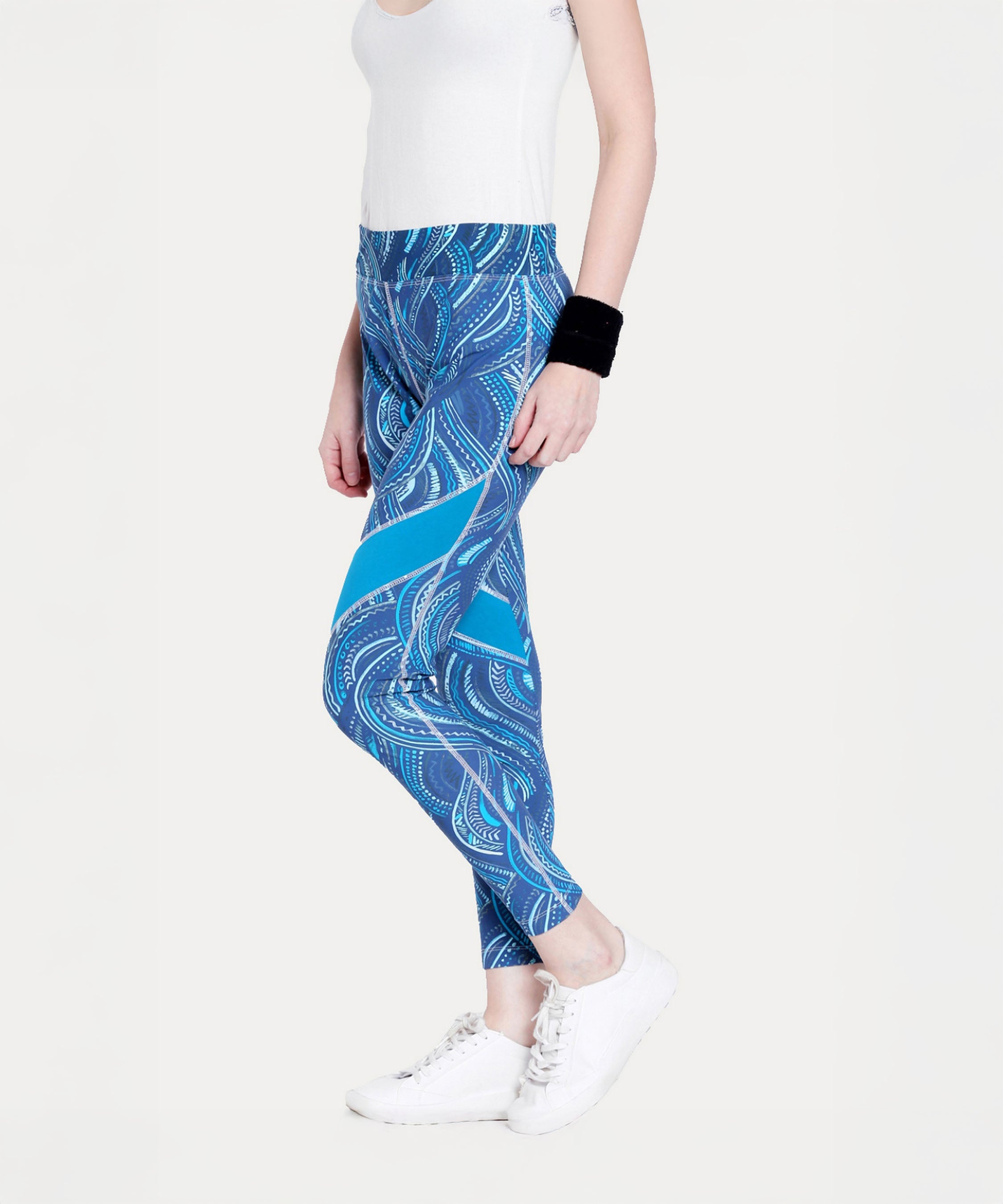 Woman wearing Tuna Active Printed Blue Leggings, a white tank top, white sneakers, and a black wristband.