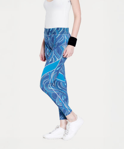 Woman wearing Tuna Active Printed Blue Leggings, a white tank top, white sneakers, and a black wristband.