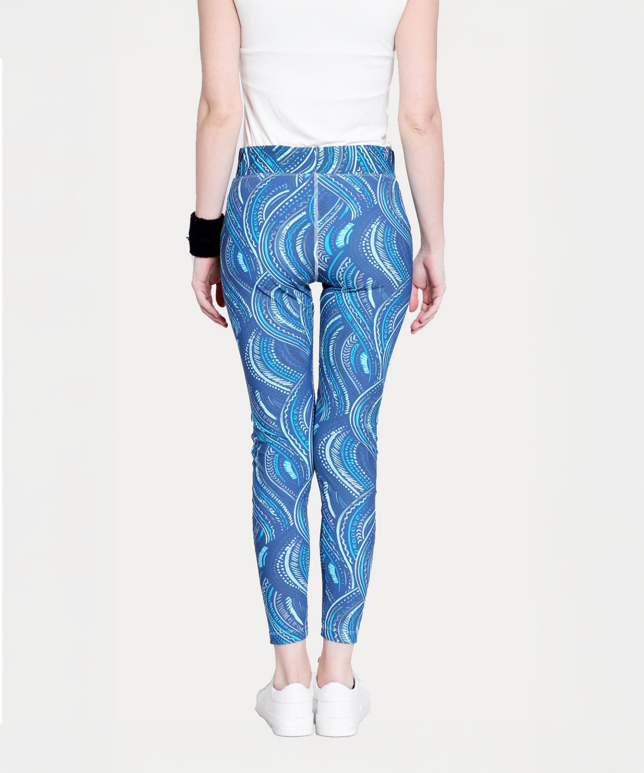 Person wearing Tuna Active Printed Blue Leggings, a white top, white shoes, and a black wristband, shown from the back.