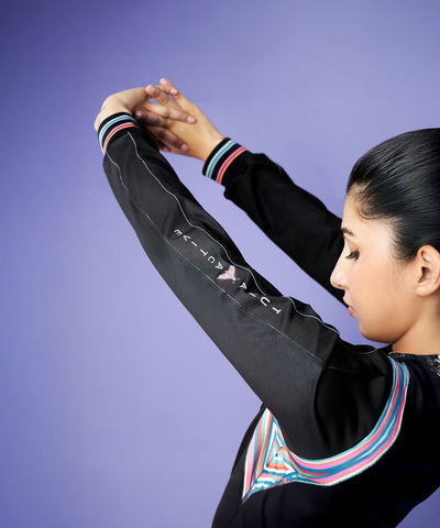Woman stretching her arms overhead, wearing the Tuna Active Black Bomber Jacket with colored stripes, against a purple background.