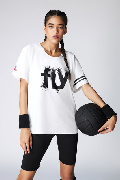 A woman in sportswear holds a black volleyball, wearing the Oversize Fly Tee made from 100% cotton paired with black shorts.