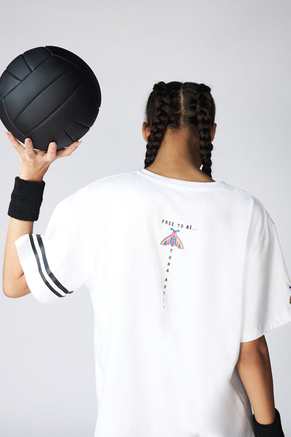 A person with braided hair holds a black volleyball, wearing the Oversize Fly Tee—an oversized 100% cotton T-shirt featuring a small butterfly print graphic on the back.