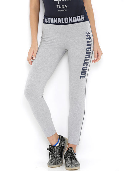 Someone wears Narrow Fit Track Pants in grey with "#TUNALONDON" and "#FITGIRLCODE" prints, paired with black sneakers for extra comfort.